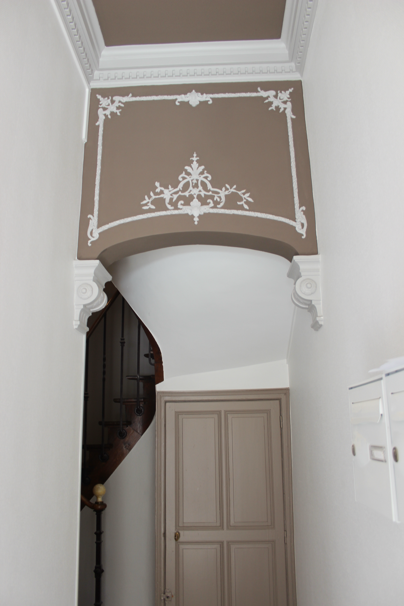 Entrée de l'immeuble : arc ornemental, plâtres et escalier en bois
